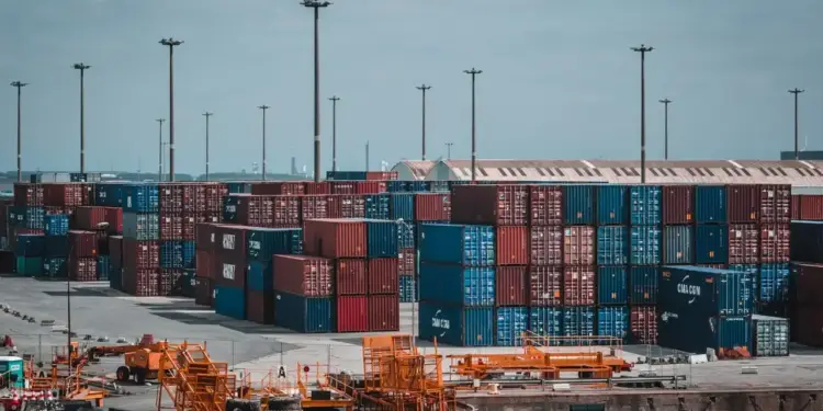 Apilamiento de contenedores de carga marítima en un puerto comercial con grúas y torres de iluminación.