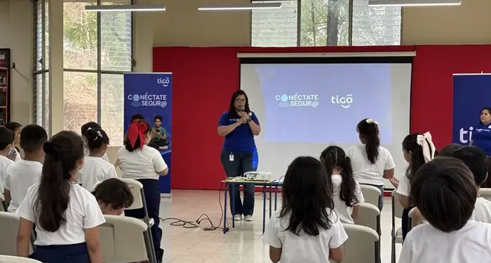 Una mujer con micrófono dando una charla frente a un grupo de niños en un salón amplio