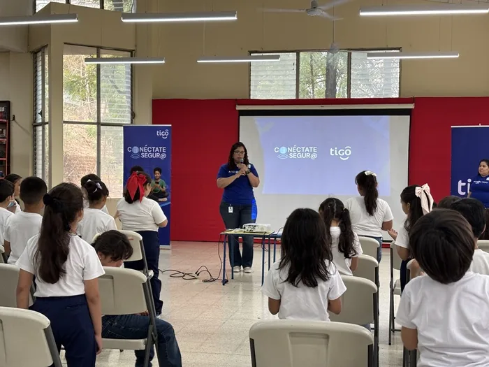 Una mujer con micrófono dando una charla frente a un grupo de niños en un salón amplio