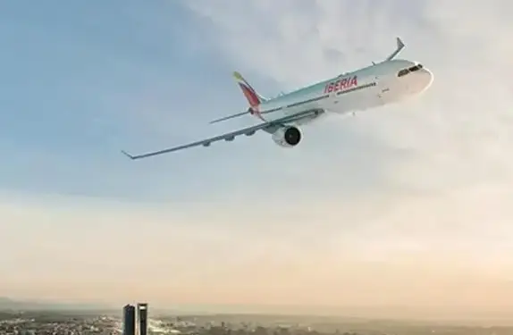 Avión de pasajeros Iberia volando sobre una ciudad con rascacielos al atardecer, simbolizando viajes de negocios y conexión global.