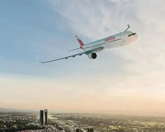 Avión de pasajeros Iberia volando sobre una ciudad con rascacielos al atardecer, simbolizando viajes de negocios y conexión global.