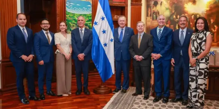 Grupo de personas en traje formal posando junto a una bandera nacional en una oficina ejecutiva.