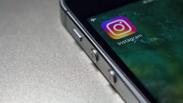 Primer plano de un smartphone oscuro mostrando la aplicación de Instagram en su pantalla táctil sobre una superficie gris