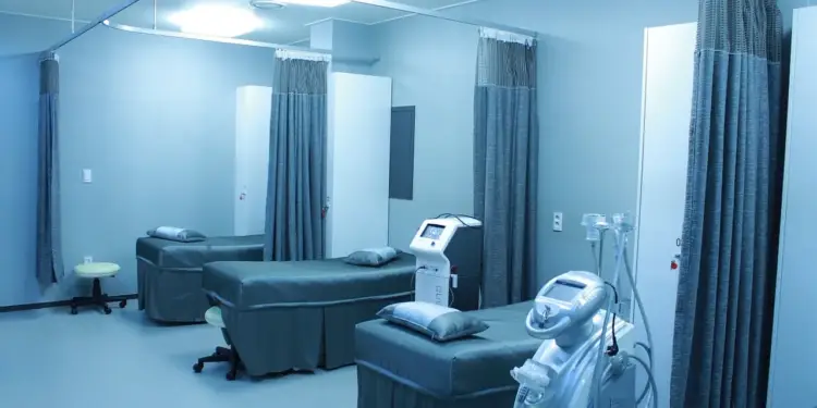Sala médica moderna con camillas, cortinas divisorias y equipos tecnológicos especializados en azul.