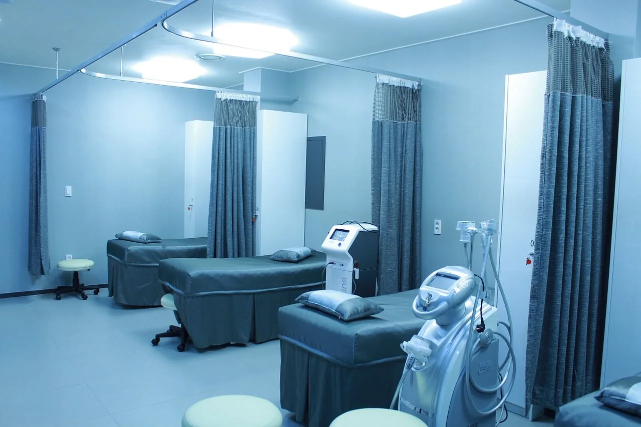 Sala médica moderna con camillas, cortinas divisorias y equipos tecnológicos especializados en azul.