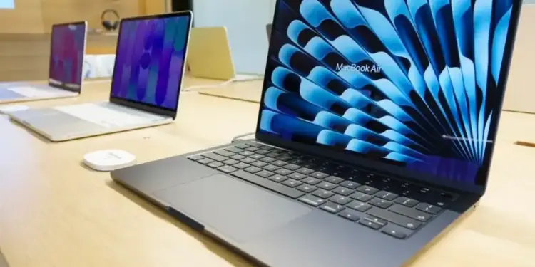 Computadoras portátiles en una mesa de madera dentro de una tienda con pantallas encendidas.