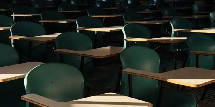 Vista general de una sala de conferencias o salón de clases con múltiples pupitres y sillas verdes vacíos.