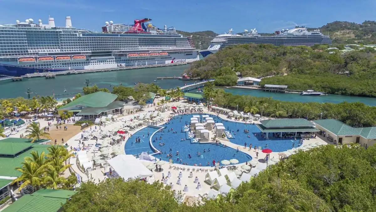 Vista aérea de un complejo turístico tropical con una gran piscina y grandes cruceros atracados en el puerto.