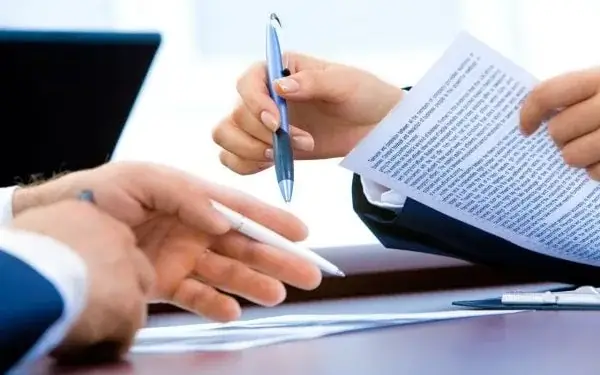 Manos de profesionales sosteniendo bolígrafos mientras revisan y firman documentos en una mesa de oficina.