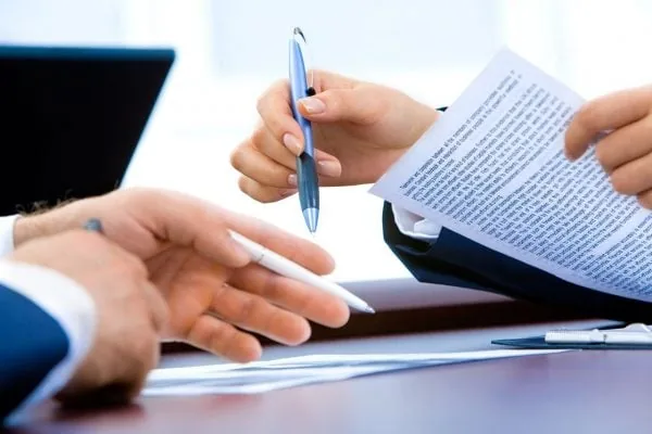 Manos de profesionales sosteniendo bolígrafos mientras revisan y firman documentos en una mesa de oficina.