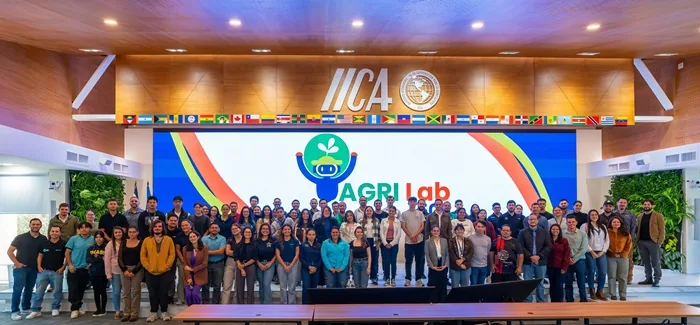Grupo numeroso de personas reunidas en un auditorio frente a una pantalla con el logotipo de AGRI Lab y banderas.