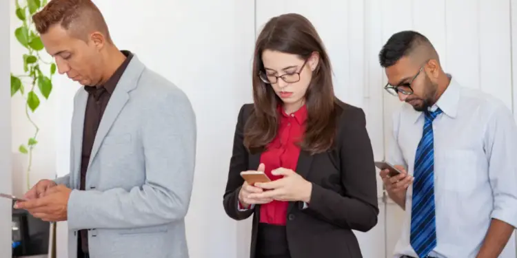 Tres profesionales de pie mirando fijamente las pantallas de sus teléfonos inteligentes en una oficina.