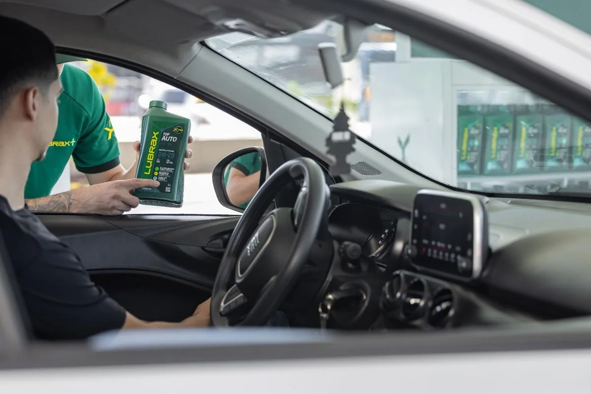 Un trabajador de una estación de servicio muestra una botella de aceite para motor al conductor de un automóvil.