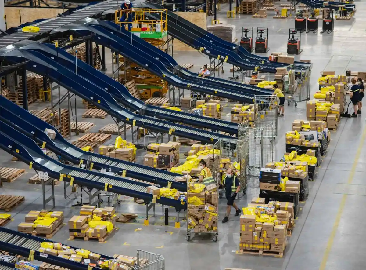 Vista aérea de un centro de distribución industrial con cintas transportadoras y trabajadores organizando paquetes.