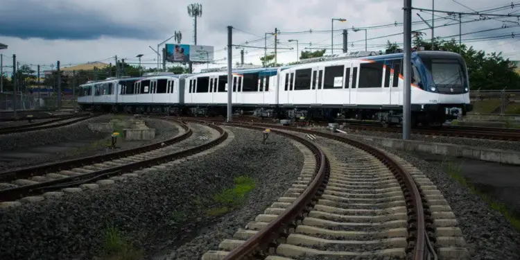 Tren moderno blanco y azul en vías férreas curvas bajo cielo nublado. Infraestructura de transporte público y desarrollo urbano.