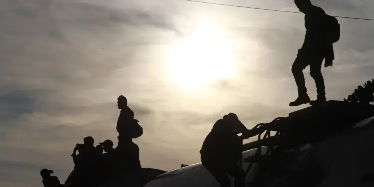 Siluetas de personas viajando en la parte superior de un tren contra un cielo brillante.
