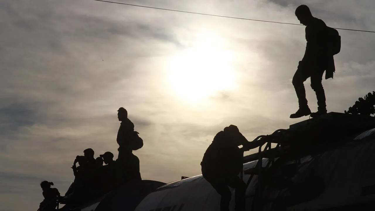 Siluetas de personas viajando en la parte superior de un tren contra un cielo brillante.