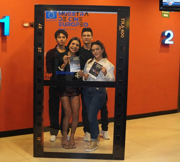 Cuatro jóvenes sonrientes posan juntos dentro de un marco decorativo con diseño de película cinematográfica en un pasillo.
