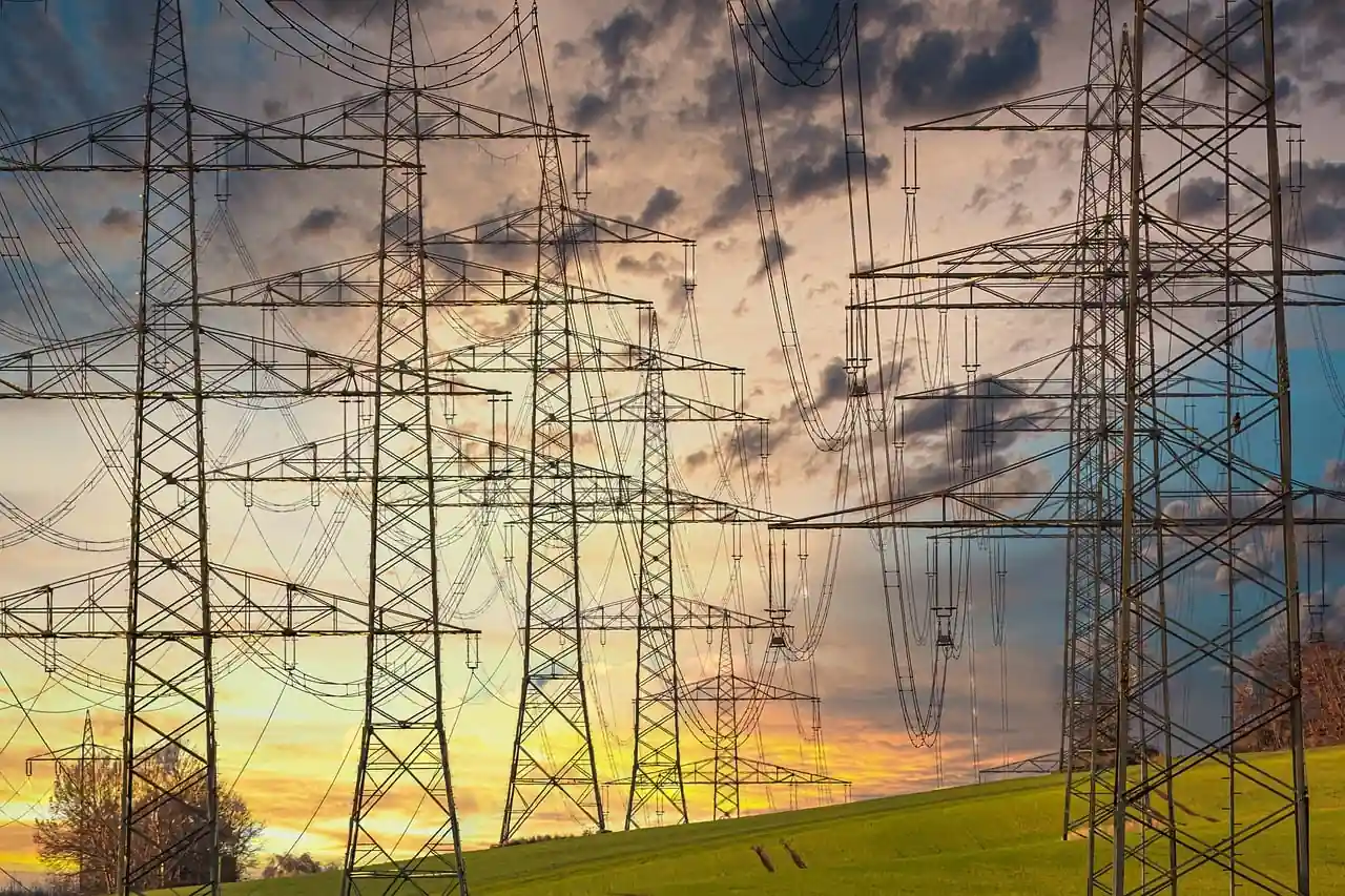 Múltiples torres de alta tensión y tendido eléctrico sobre un campo verde al atardecer.