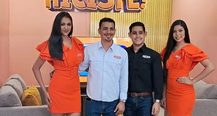 Cuatro personas, dos hombres y dos mujeres en vestimenta promocional, posan sonrientes frente a un letrero de Almacenes Tropigas y Yala.
