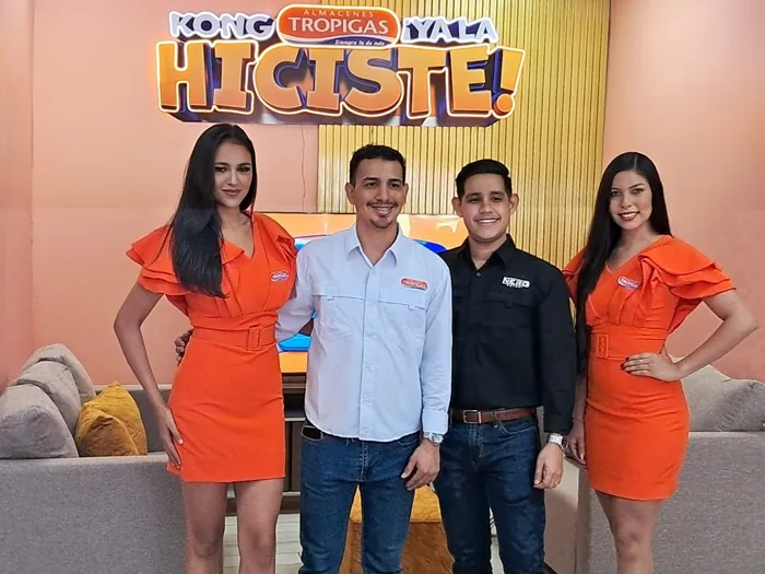 Cuatro personas, dos hombres y dos mujeres en vestimenta promocional, posan sonrientes frente a un letrero de Almacenes Tropigas y Yala.