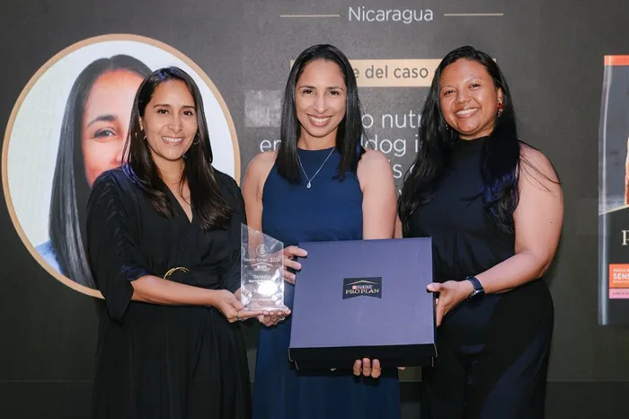 Tres mujeres profesionales sonriendo mientras sostienen un trofeo y una caja con el logotipo de Purina Pro Plan.