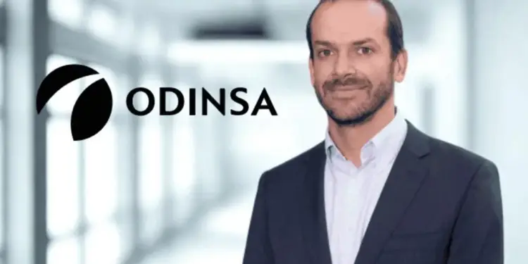 Retrato de un hombre de negocios con traje junto al logotipo de Odinsa en una oficina moderna.