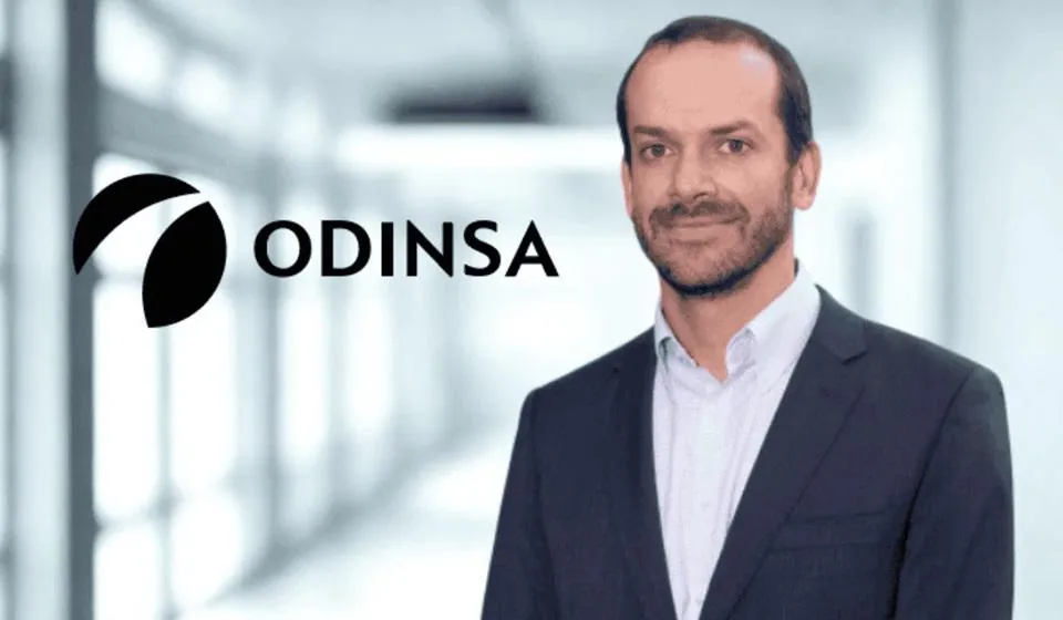 Retrato de un hombre de negocios con traje junto al logotipo de Odinsa en una oficina moderna.
