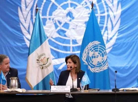 Mujer hablando en un estrado con banderas de Guatemala y de la ONU de fondo.