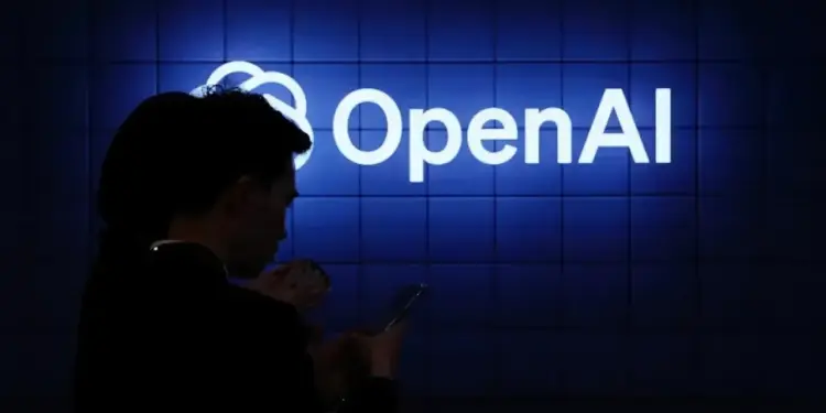 Silueta de una persona utilizando un teléfono móvil frente a un cartel luminoso con el logotipo de OpenAI en tonos azules.