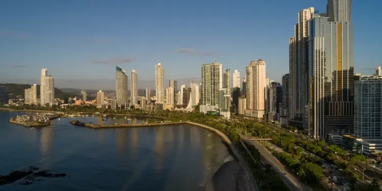 Vista panorámica de rascacielos modernos ubicados junto a una bahía y una carretera costera bajo un cielo azul.