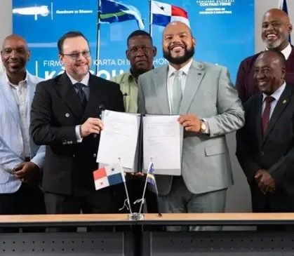 Un grupo de hombres de negocios sonríe mientras dos de ellos sostienen documentos para firmar un acuerdo, con banderas de Panamá y otro país al frente.