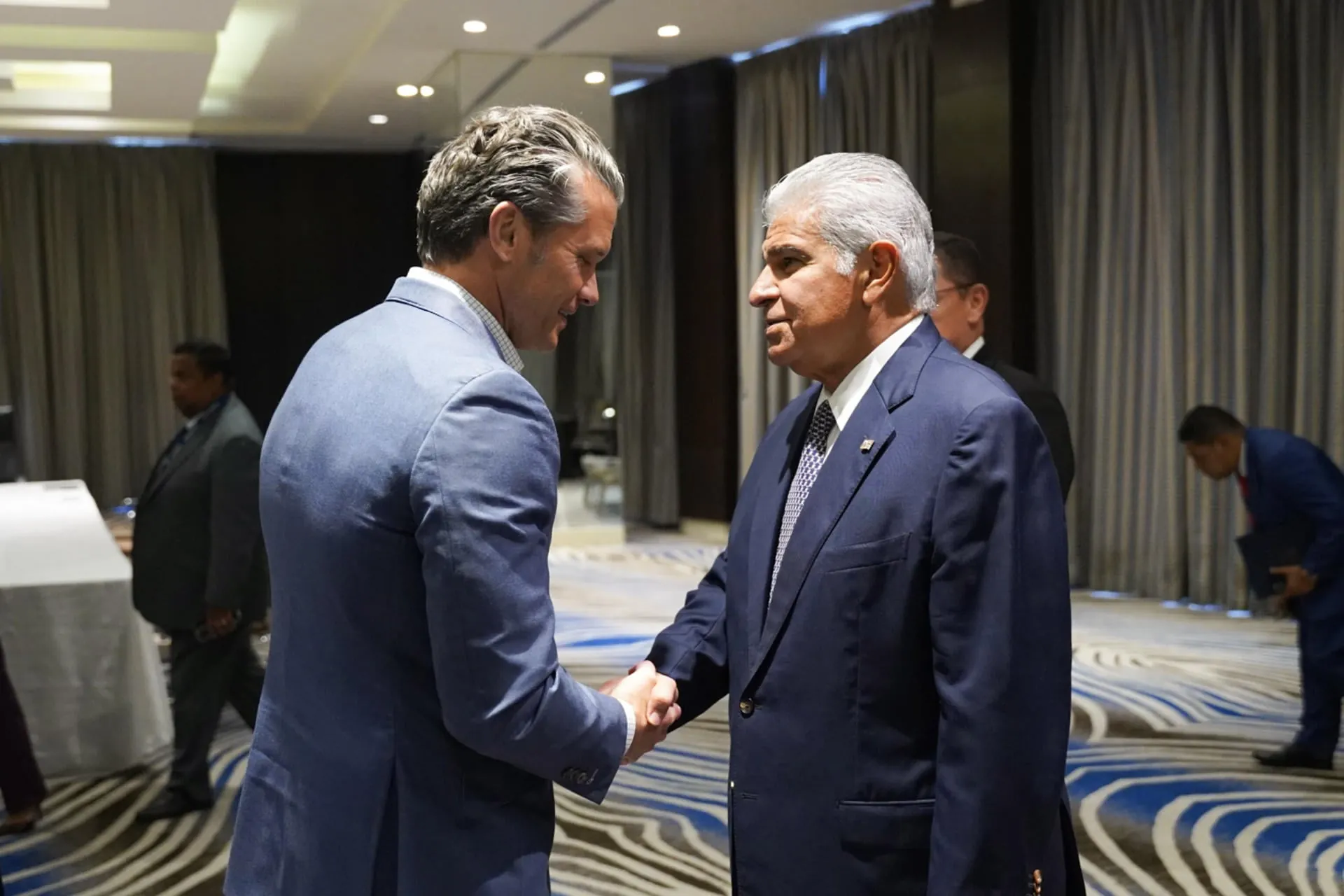 Dos hombres con traje formal estrechándose la mano en un salón de eventos corporativo