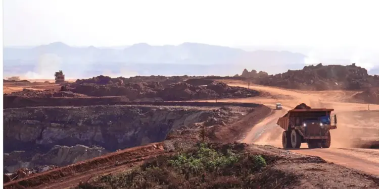 Camión de minería de gran tamaño transitando por un camino de tierra en una mina a cielo abierto con montañas de fondo.