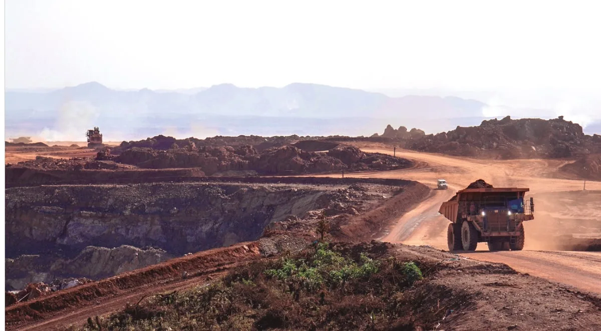 Camión de minería de gran tamaño transitando por un camino de tierra en una mina a cielo abierto con montañas de fondo.