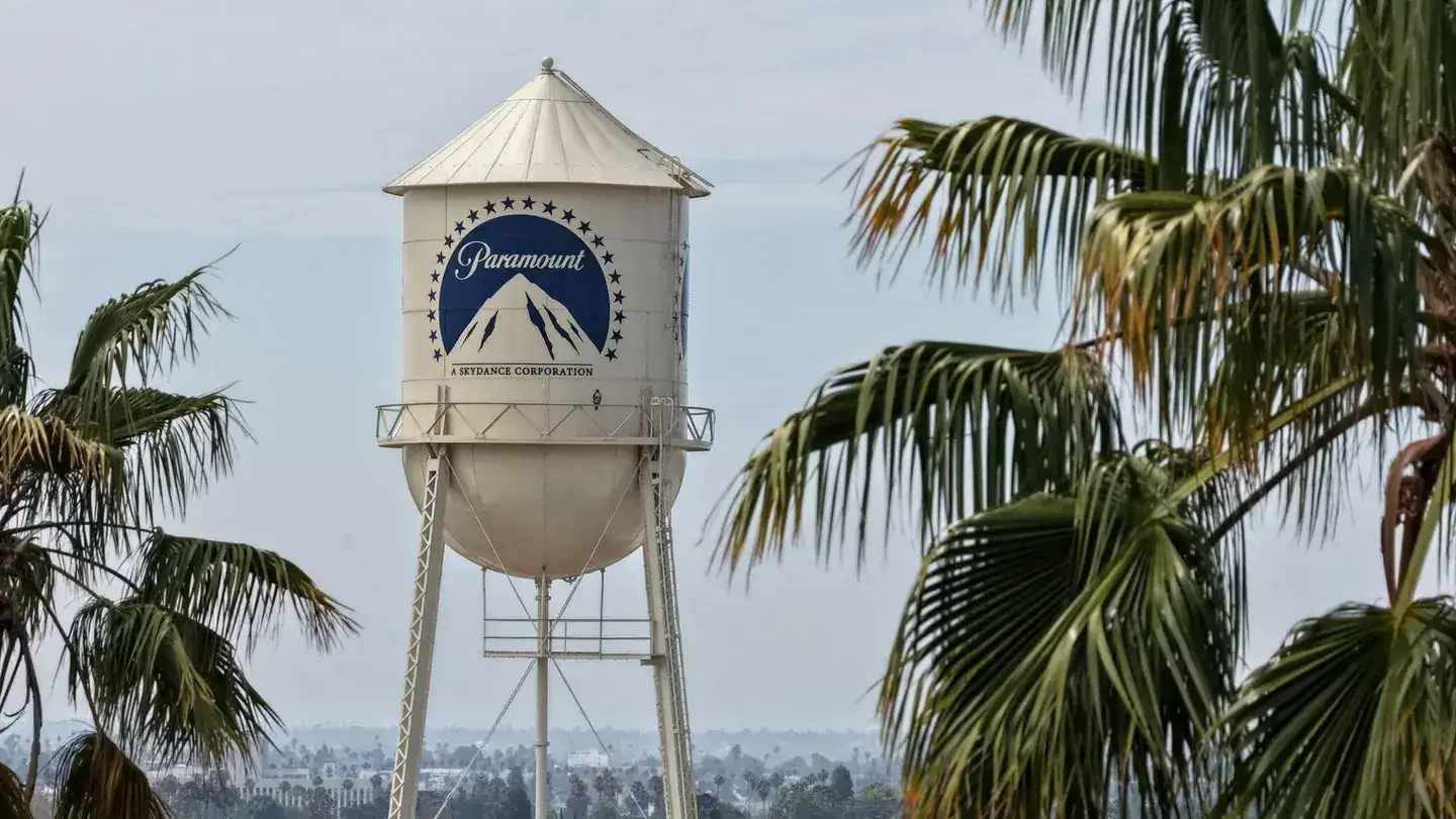 Torre de agua blanca con el logotipo azul de Paramount rodeada de palmeras en un entorno urbano.