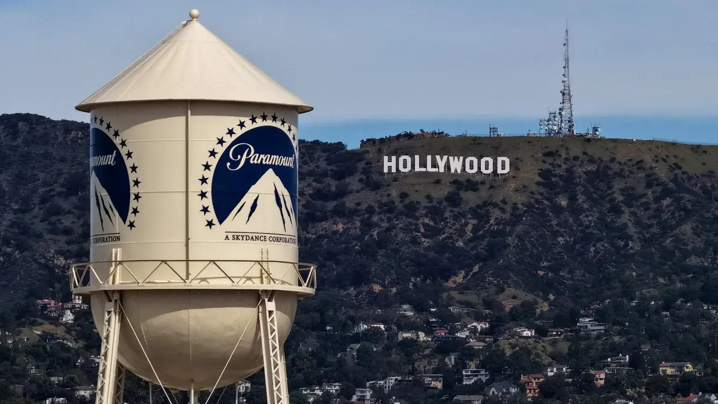 Torre de agua corporativa en primer plano con el cartel de Hollywood en una colina al fondo.