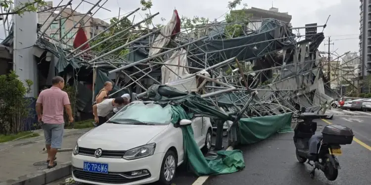 Vista de una estructura de andamios y lonas verdes derrumbada sobre un vehículo blanco en una calle urbana, con tres personas evaluando los daños.
