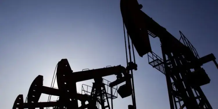 Siluetas de varios balancines de extracción de petróleo contra un cielo azul claro. Las estructuras industriales se ven oscuras por el contraluz.
