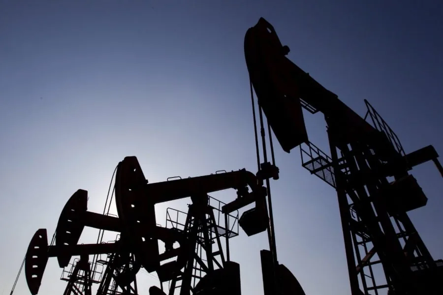 Siluetas de varios balancines de extracción de petróleo contra un cielo azul claro. Las estructuras industriales se ven oscuras por el contraluz.