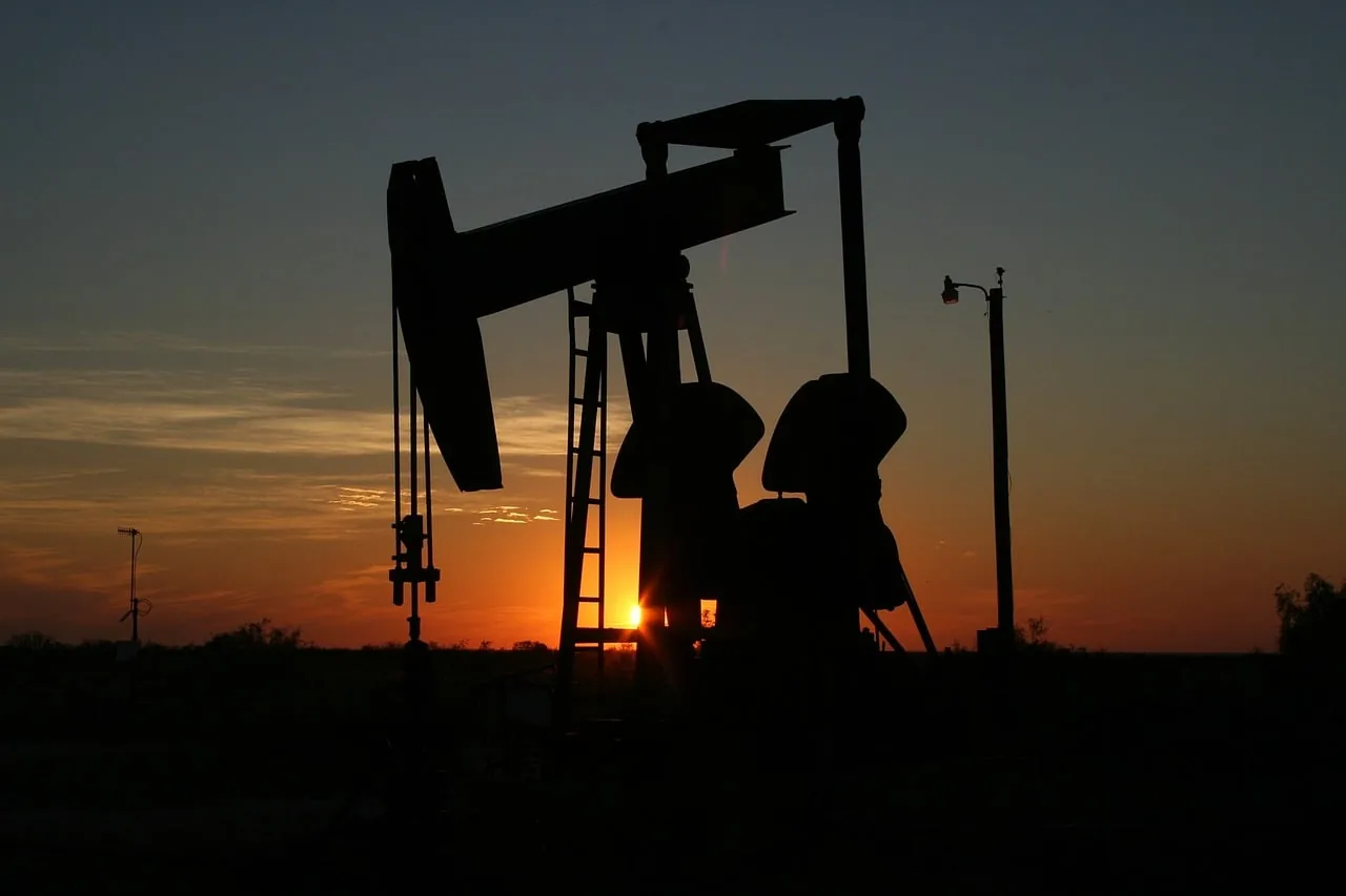 Silueta de una bomba de balancín extrayendo petróleo al atardecer, con el sol naranja brillante en el horizonte. Representa la industria energética y el mercado global de hidrocarburos.