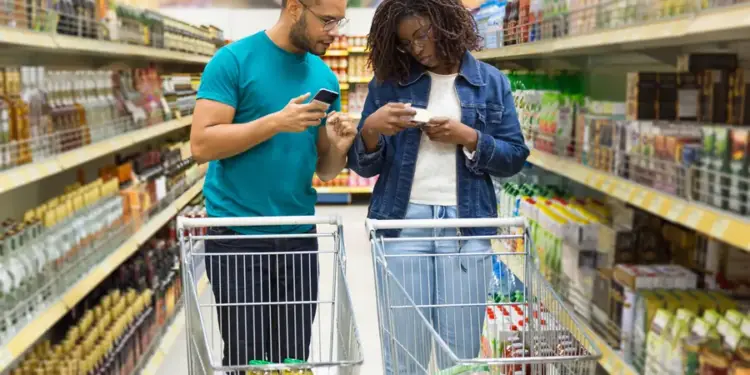 Pareja joven con carritos de compras revisando productos en el pasillo de un supermercado.