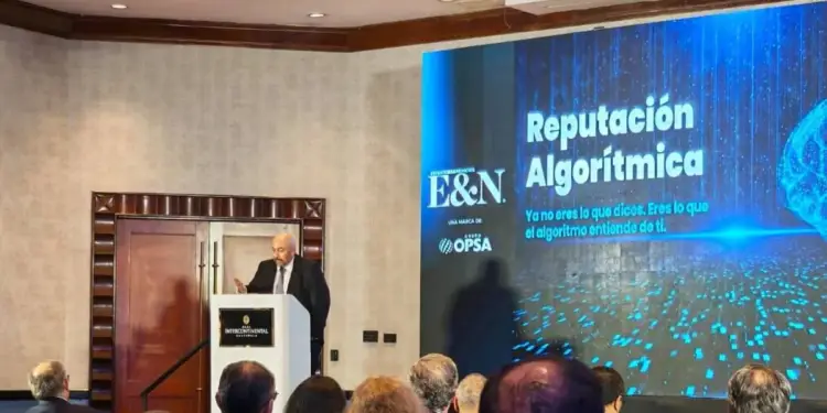 Hombre en traje dando una conferencia en el Hotel Intercontinental Guatemala sobre reputación algorítmica ante una audiencia. Pantalla muestra texto y logo E&N.