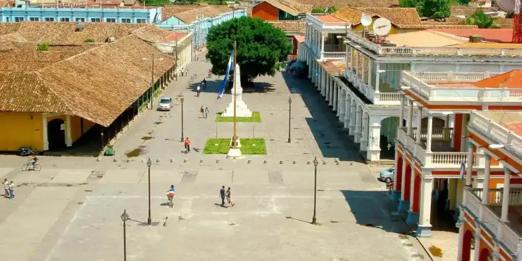 Vista aérea de una plaza central rodeada de edificios coloniales con techos de tejas y soportales en un día soleado.