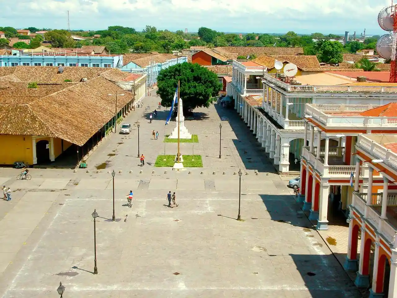 Vista aérea de una plaza central rodeada de edificios coloniales con techos de tejas y soportales en un día soleado.