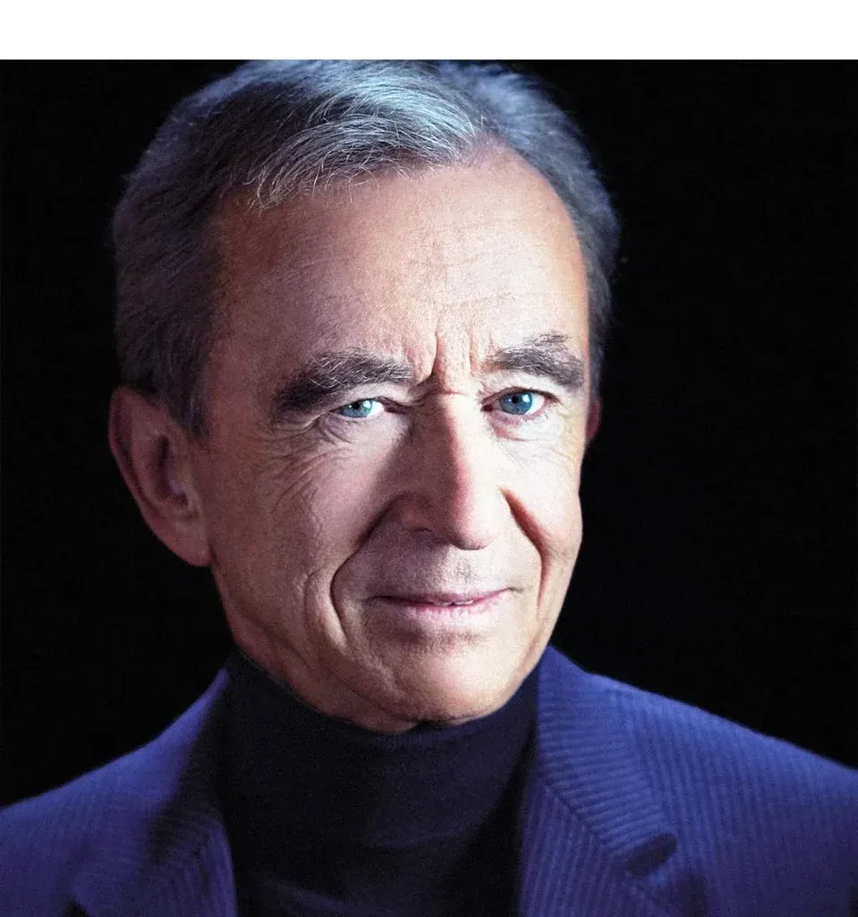 Retrato de un hombre mayor con cabello gris, ojos azules, vistiendo un blazer azul oscuro y cuello alto negro, mirando al frente con una leve sonrisa.