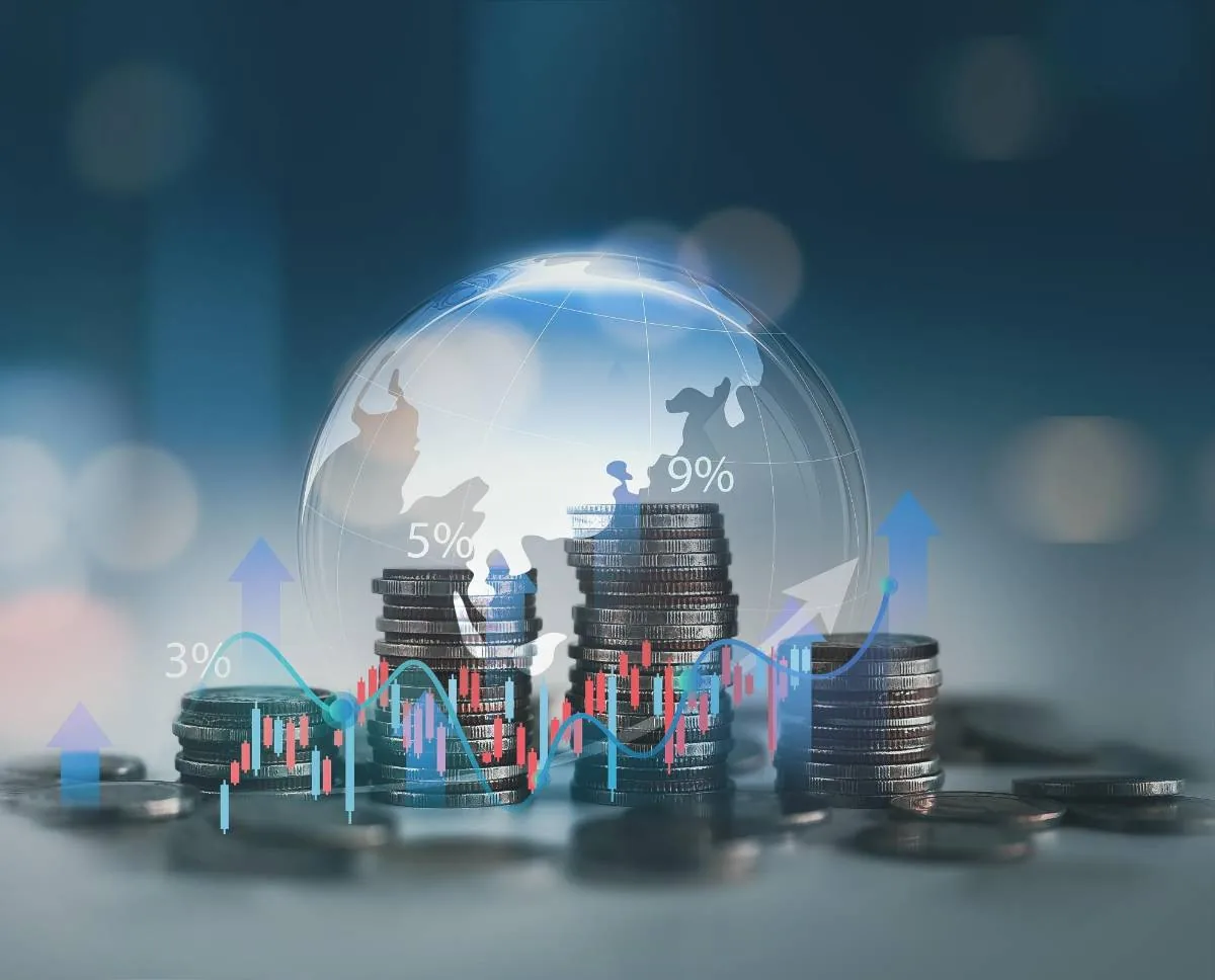 Montones de monedas apiladas con un globo terráqueo transparente y gráficos financieros superpuestos.