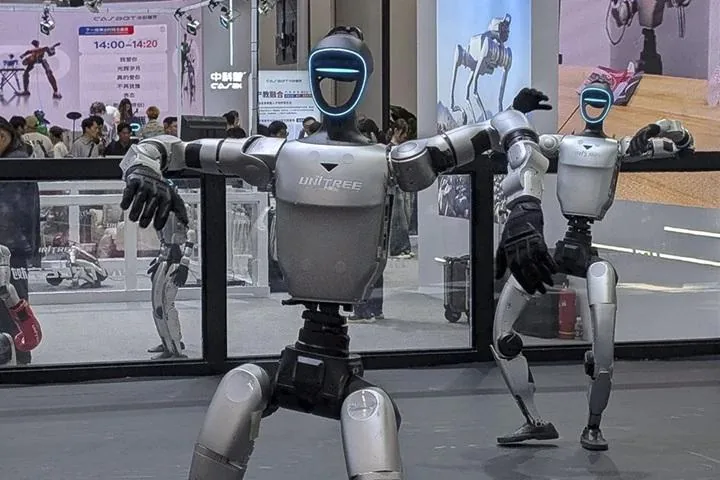 Dos robots humanoides de pie y con luces azules en la cabeza en una feria tecnológica, mostrando avances de la robótica.
