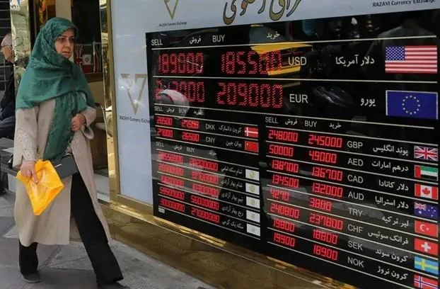 Una mujer con velo verde y abrigo beige mira un tablero electrónico que muestra tasas de compra y venta de divisas extranjeras como USD, EUR, GBP, AED, CAD, AUD, TRY, CHF, SEK y NOK.