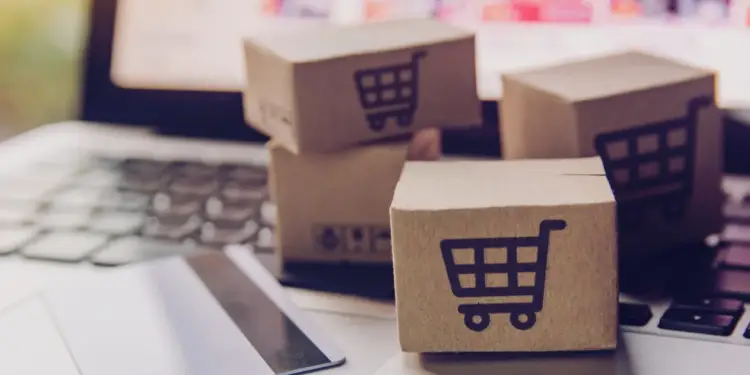 Cajas de cartón con símbolo de carrito sobre teclado de laptop junto a una tarjeta bancaria.